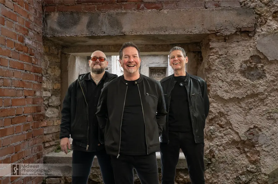 Q Sonics standing together in front of a brick and stone wall